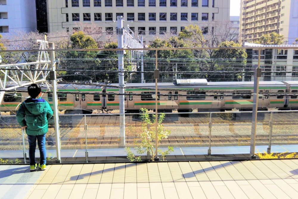 カワサキデルタ｜線路沿いデッキから見える東海道本線の電車と電車を眺める子供