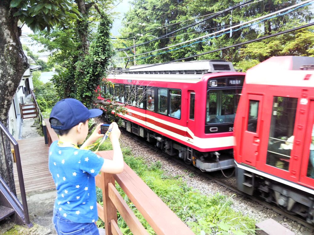 箱根登山電車が見えるスイッチバックカフェ｜デッキから見える箱根登山電車（アレグラ号）スイッチバック前（箱根湯本駅から強羅駅方面へ）写真を撮る子供